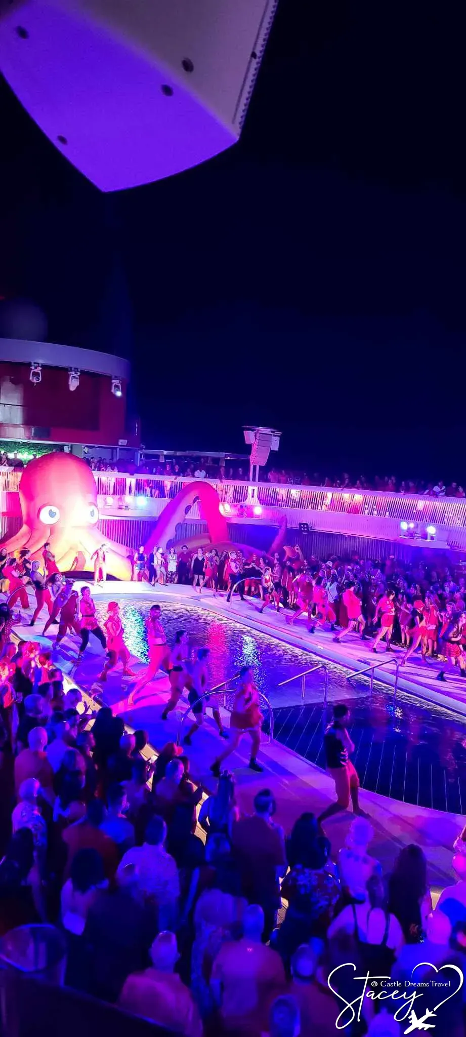 Nighttime pool-deck party on a Virgin Voyages ship with performers, crowds, and a giant inflatable octopus