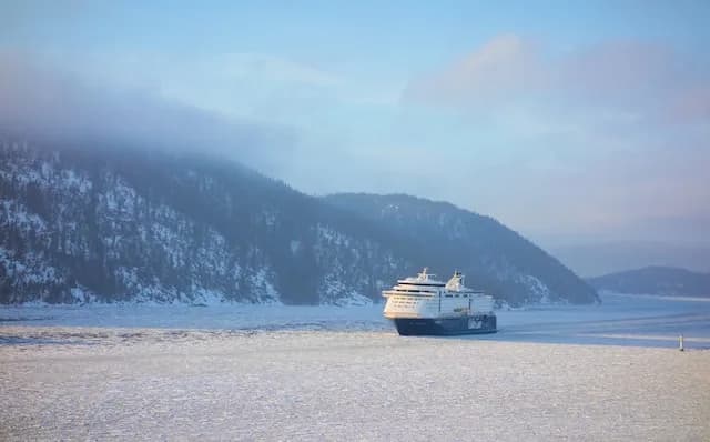 Cruise ship sailing an icy fjord between snow-dusted mountains
