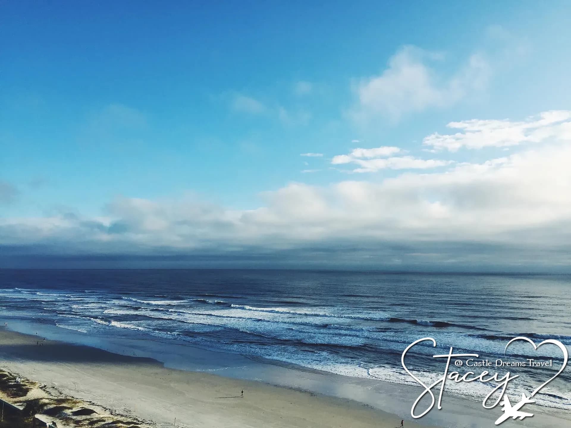 Waves rolling onto the wide sandy shoreline of Daytona Beach under a blue sky