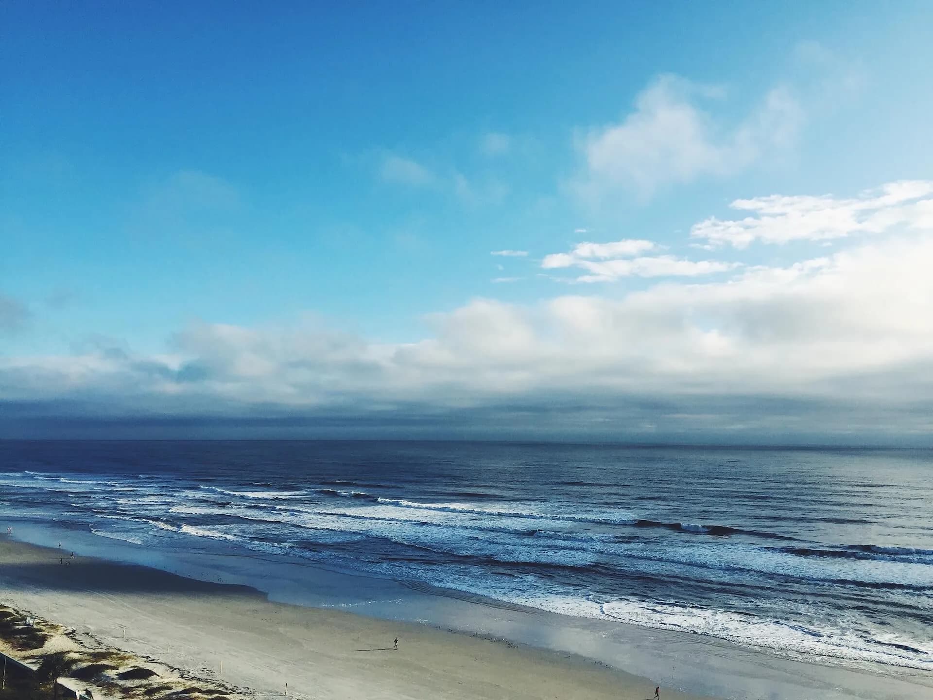 Waves rolling onto the wide sandy shoreline of Daytona Beach under a blue sky