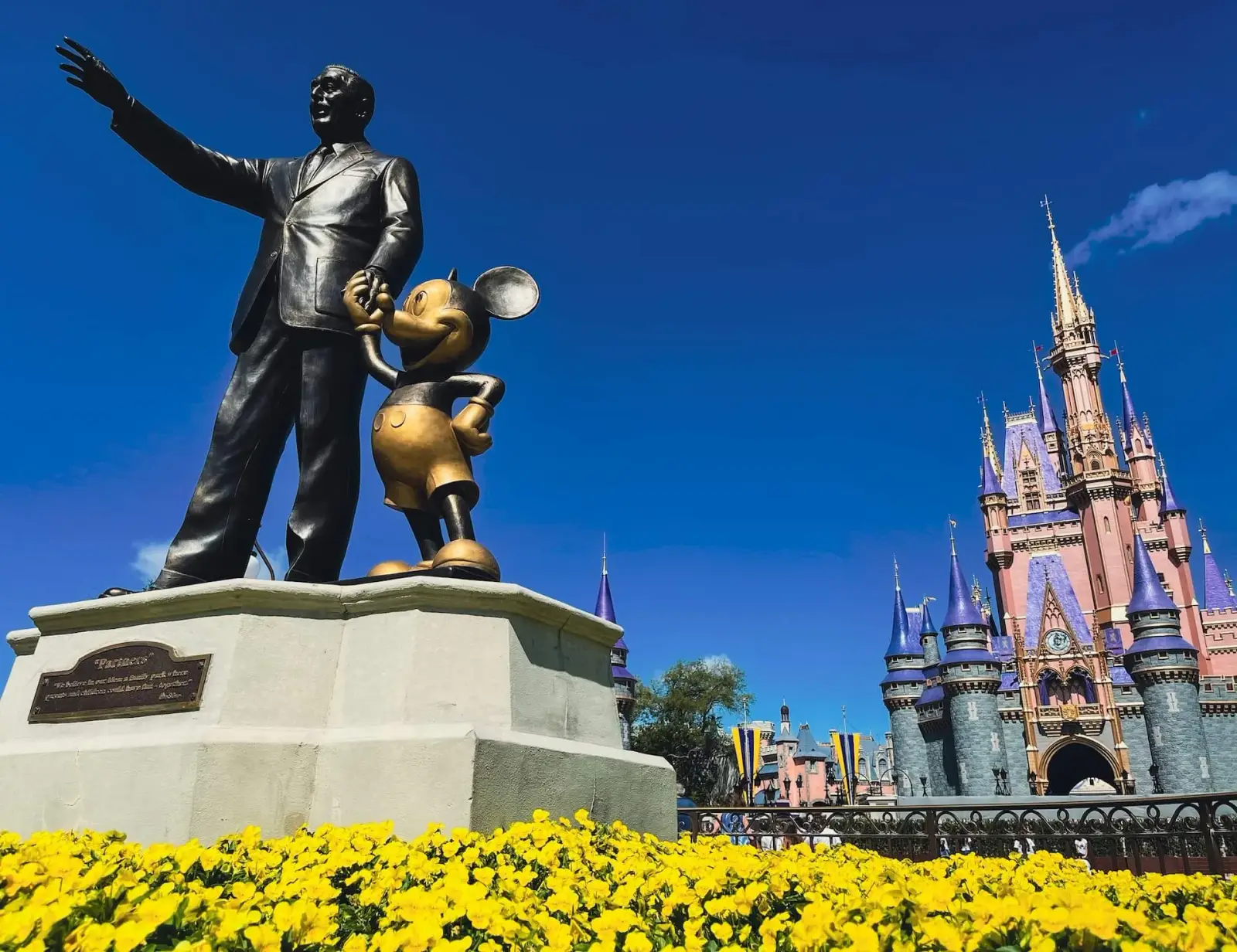 Partners statue of Walt Disney and Mickey Mouse in front of Cinderella Castle at Magic Kingdom, with yellow flowers in bloom