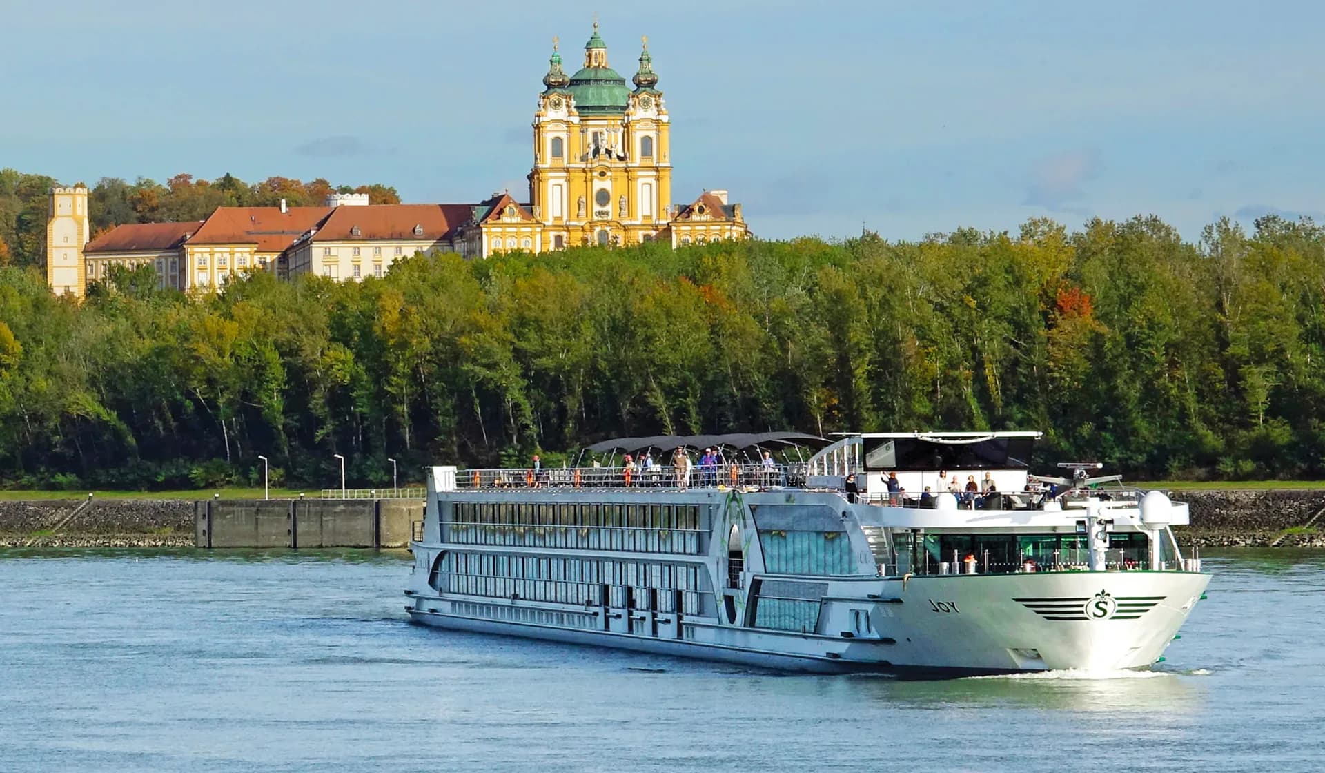 River cruise ship on the Danube passing below a hilltop baroque abbey